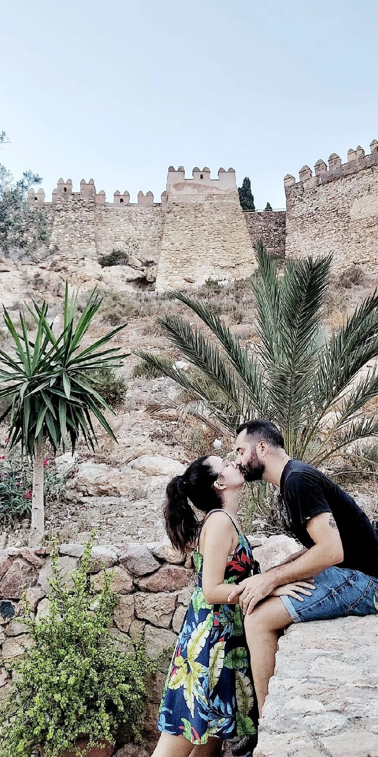 Raissa e Jesús compartilham um doce beijo em frente à majestosa fachada do Alcazaba de Almería. Ao mesmo tempo, planejam os destinos por descobrir em Almería, ansiosos para explorar os pontos de interesse desta cidade andaluza.